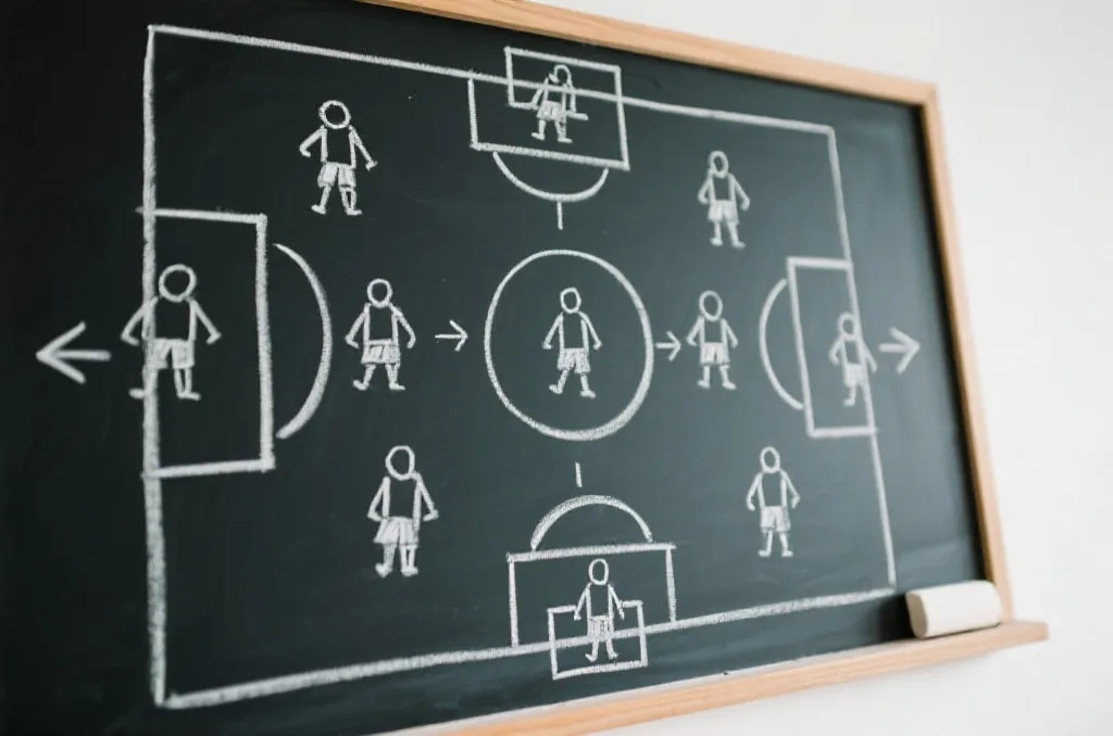 A tactical soccer chalkboard with white chalk drawings of player formations and strategic arrows